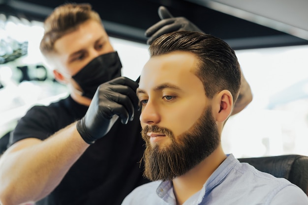 Парикмахер или парикмахер расчесывает волосы мужчине, делая прическу в современной парикмахерской