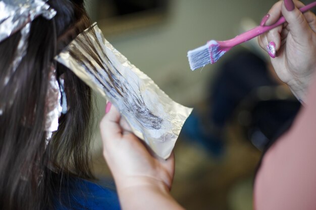 The hairdresser paints a brunette woman's hair in the beauty salon