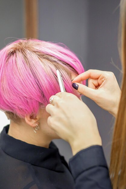 美容師は、若い女性の染めた短いピンクの髪を美容院での手続きに備えます。