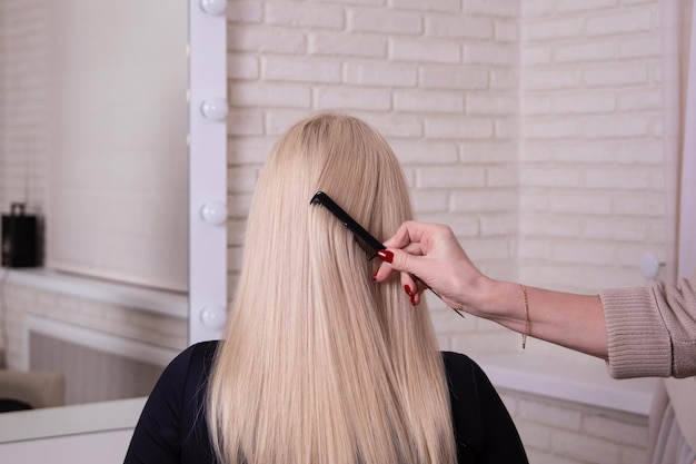 Hairdresser's hand brushing long blonde hair in beauty salon