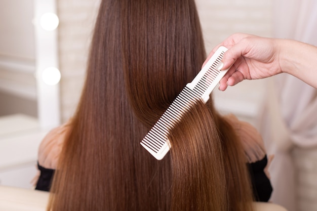 Hairdresser's hand brushing long brunette hair in beauty salon