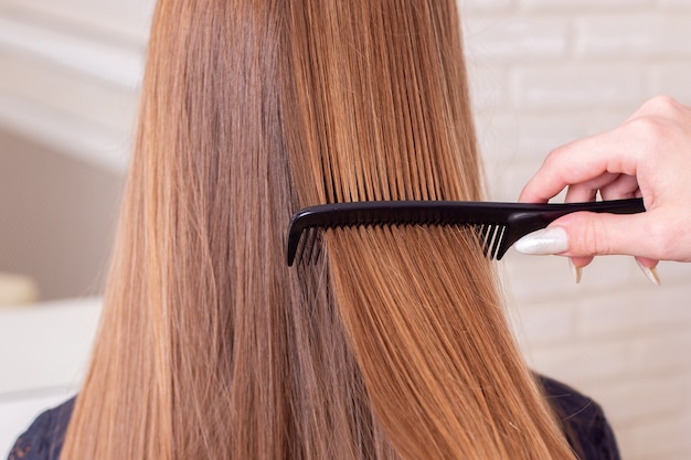 La mano del parrucchiere che spazzola i capelli lunghi del brunette