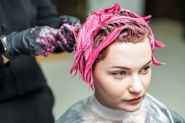 Photo hairdresser's hands are applying pink color to customer's hair.