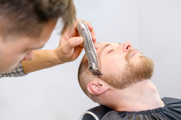 hairdresser shaves his client's beard with an electric trimmer.