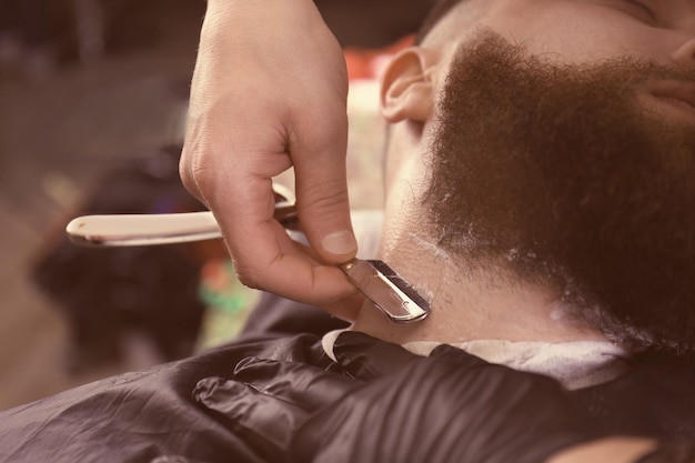 Hairdresser shaving client in barbershop