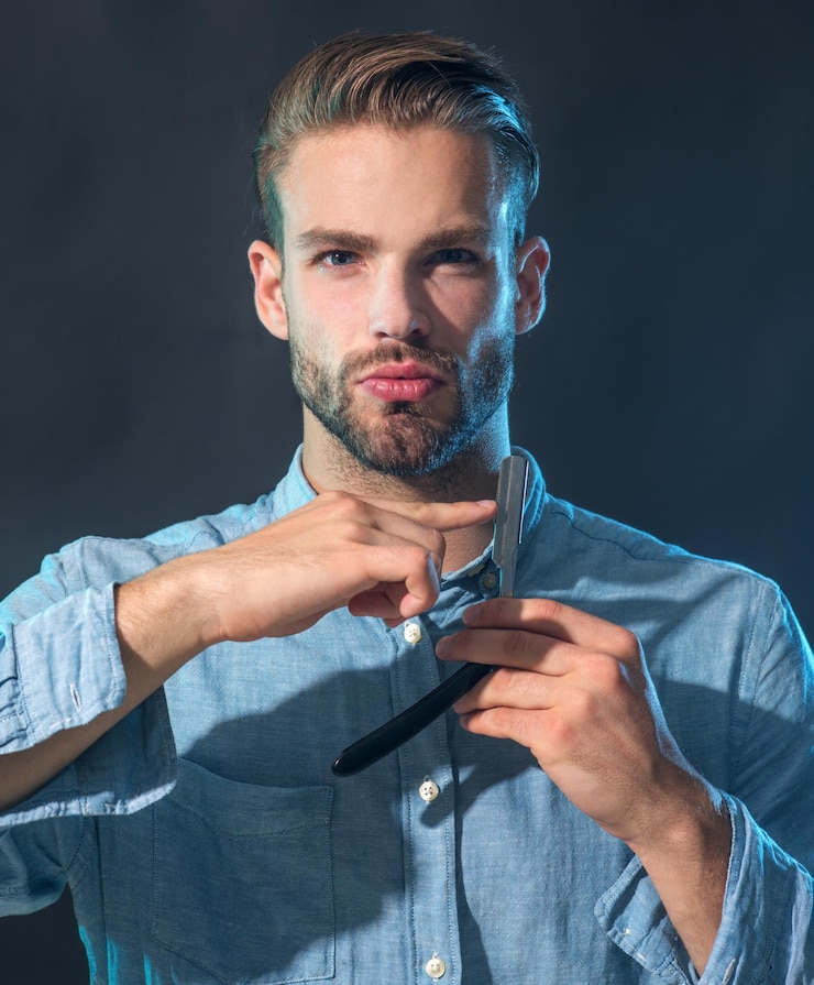 फोटो hairdresser in stylish shirt demonstrating sharp blade of his straight razor for shaving tool for barber or shave brutal hipster in casual wear with vintage straight razor barbershop accessories