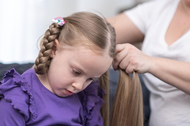 Hairdresser stylist brushing child girl blond hair and styling hairdo braid hairstyle getting ready