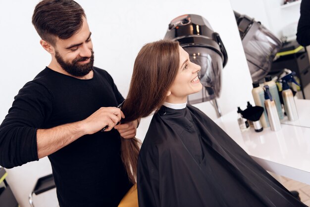 Hairdresser stylist is combing young woman with brown hair