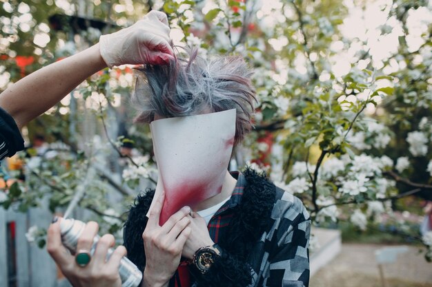 Hairdresser stylist makeup artist dyes the hair of a young man with a closed face from an aerosol can