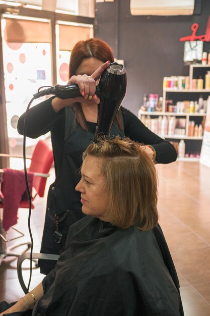 Hairdresser uses a hairdryer and styles a hair of a woman