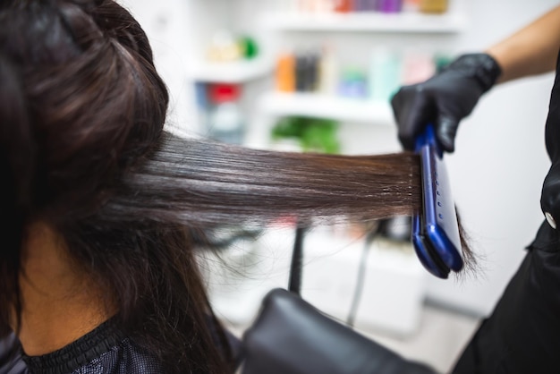 Parrucchiere che utilizza un capello stirato per raddrizzare i capelli parrucchiere che lavora sull'acconciatura di una donna al salonecura dei capelli bella donna attraente in un salone di bellezza