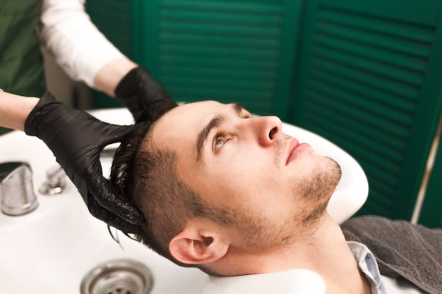 Hairdresser washes a client’s hair before cutting. Serious handsome man washes his head in a beauty salon