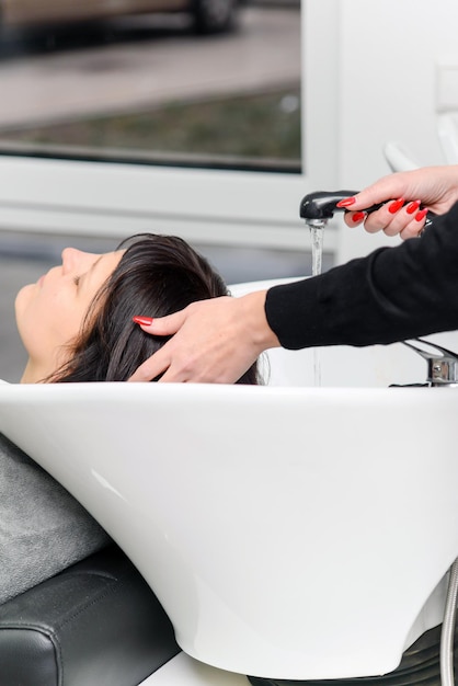 The hairdresser washes the hair of the client in the salon, medium side view, close-up, beauty conce