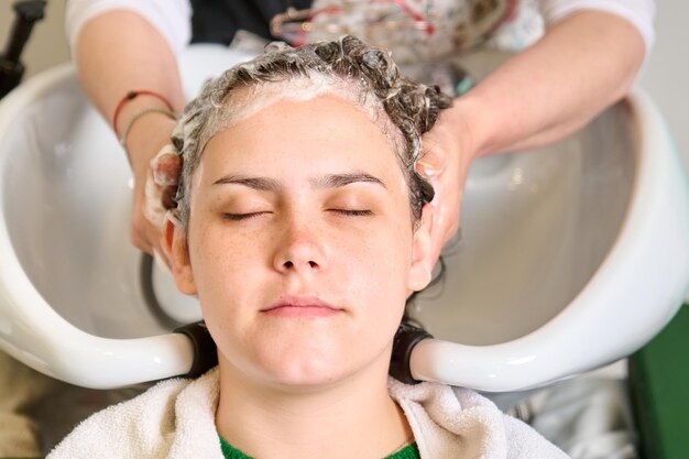 Hairdresser washes the head of a brunette girl with shampoo in\
the beauty salon