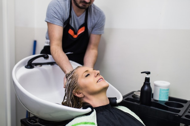 Hairdresser washing hair of a beautiful mature woman in hair salon.