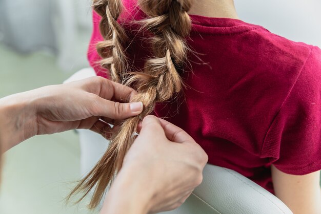 美容師が美容とヘアサロンでプレティーンのブロンドの女の子に三つ編みを織る