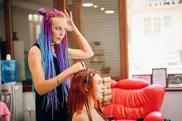 La parrucchiera intreccia le trecce afro rosse e rosse e parla con le sue trecce da barbiere dreadlock...