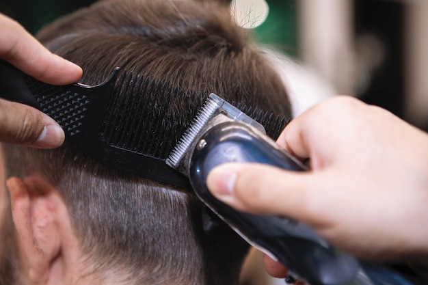 Parrucchiere con un tagliatore di capelli taglia un uomo barbuto su una sedia in un salone di barbiere