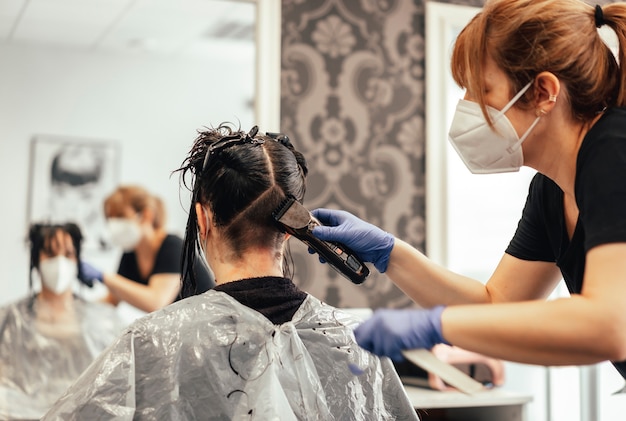 Hairdresser with mask and gloves shaving with razor. Reopening with security measures of Hairdressers in the Covid-19 pandemic