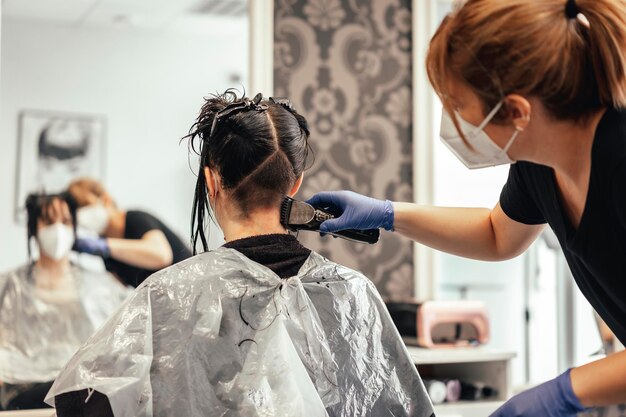 Hairdresser with mask and gloves shaving with razor