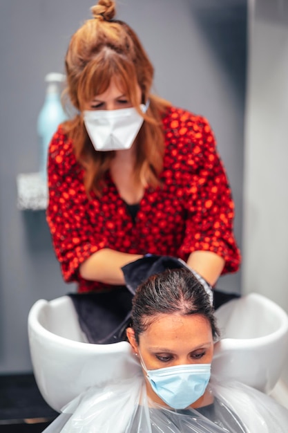 Hairdresser with mask and gloves washing the client's hair with hot tap water and soap