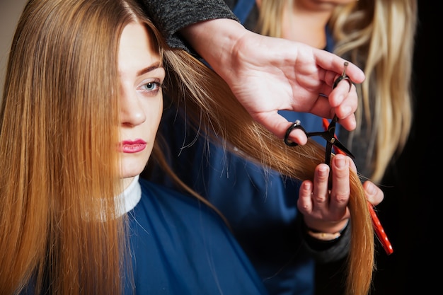 Hairdresser with scissors and comb cute hair to young woman.