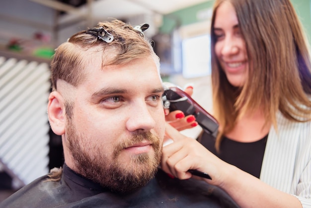 Parrucchiere donna che taglia i capelli di un uomo in un barbiere