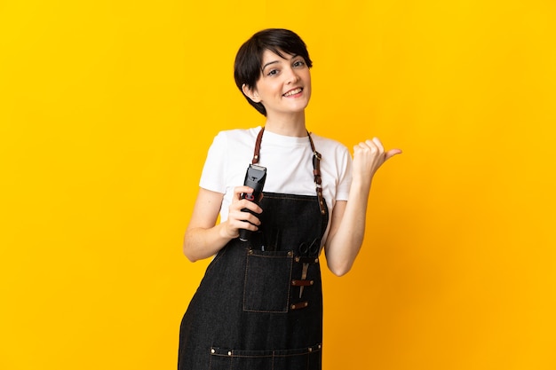 Hairdresser woman isolated on yellow wall pointing to the side to present a product