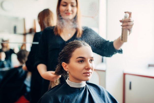 美容師はヘアスプレー、美容院の女性クライアントで動作します