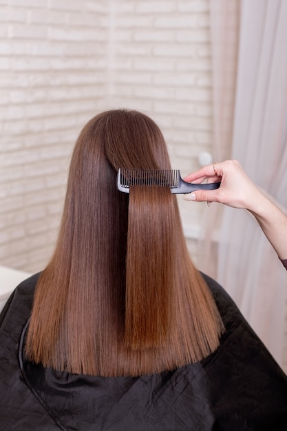 Hairdressers hand brushing long brunette hair in beauty salon