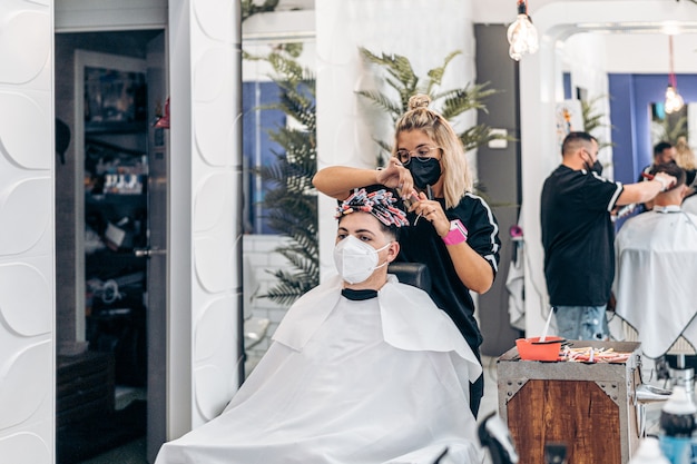 Hairdressing salon with two workers cutting and fixing the hair of two costumers sitting on a chair