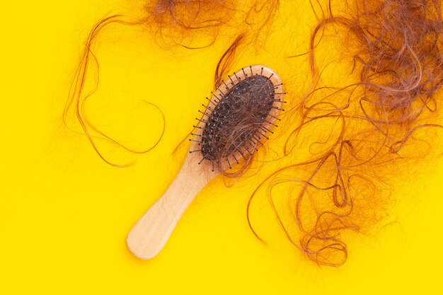 Foto caduta di perdita di capelli in pettini su sfondo giallo.