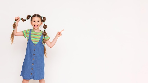 Hairstyles for children A little girl holds a braid of hair and points to your advertisement on a white isolated background copy space