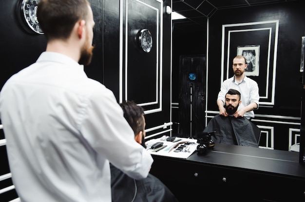 Hairstylist cuts hair and beard of man in the barbershop