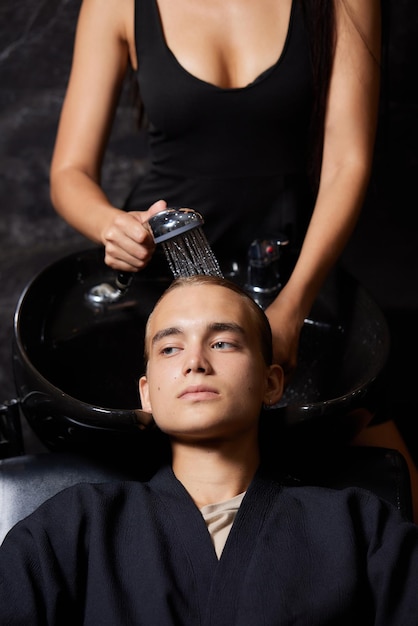 Hairstylist hairdresser washing customer hair  young man relaxing in hairdressing beauty salon