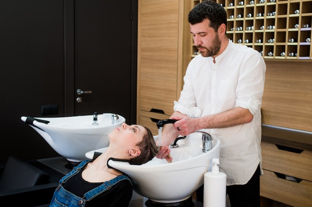 Hairstylist washing head to the young woman at the hairdresser