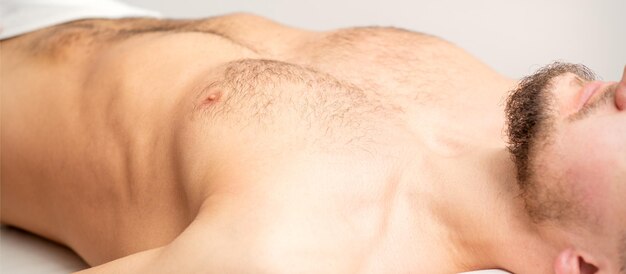 Hairy body, stomach, and chest of a man lying before epilation.