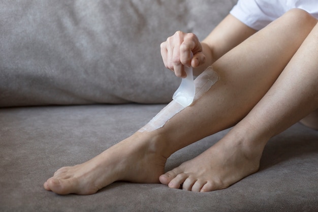 Gambe pelose femminili con crema depilatoria, primo piano. epilazione delle gambe a casa