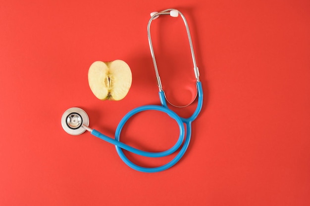 Half an apple and a medical stethoscope on a bright red background proper nutrition for diseases of the heart and respiratory tract