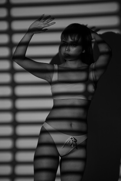 Half body Asian Woman 20s wear Bikini stay in shade of shadow from chick window curtain and express feeling alone lonely or broken heart Monochrome black and white tone