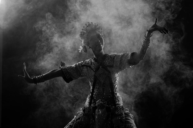 Half body of asian woman wear thai traditional costume dancer\
dress silhouette shadow khon dance is act play royal of thailand\
over black background smoke