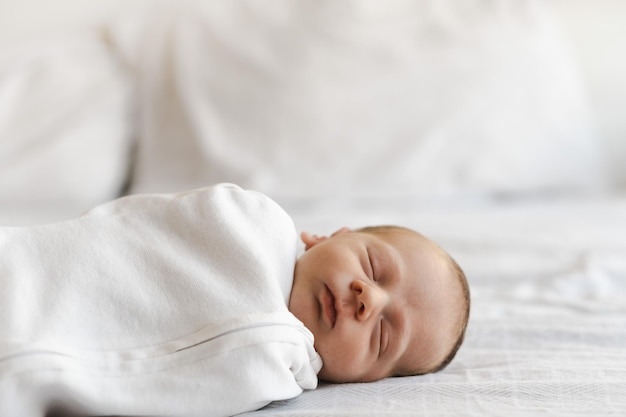 Half body shot of caucasian hairy brunet cute newborn baby sleeping wearing white drawsheetone or tw