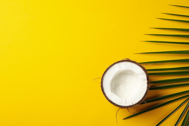 Half of coconut and palm leaf on yellow, top view