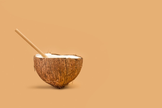 Half coconut with a disposable paper straw on a brown background  with copy space