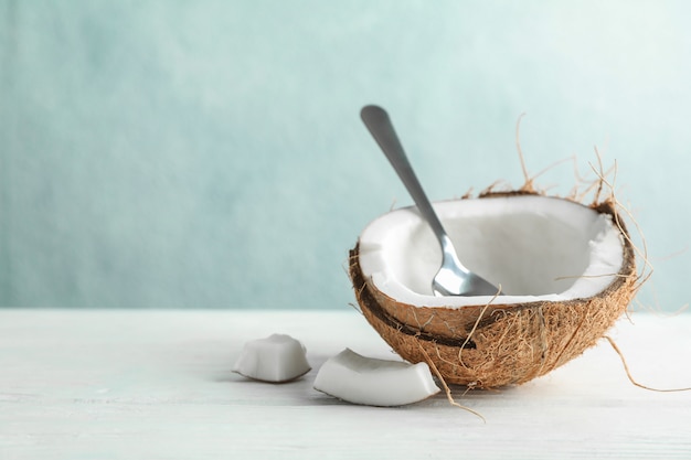 Half coconut with spoon on wooden table against grey