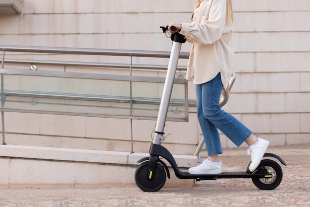 周りに建物がある市内中心部の周りで電動スクーターに乗っている認識できない若い女性の半分のトリミングされたビュー