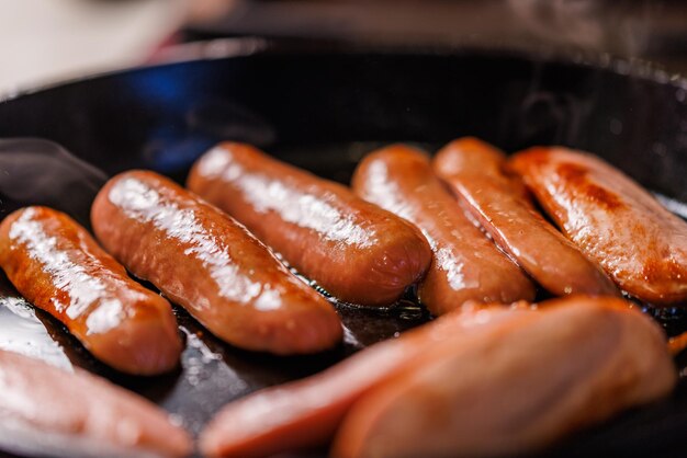Photo half-cut sausages are fried in oil in a black cast iron skillet