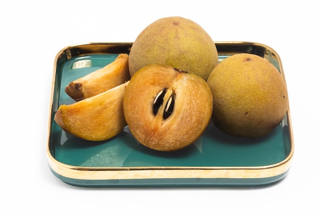 Half cut sliced and two whole fresh sapodilla fruit in a green plate isolated on white background