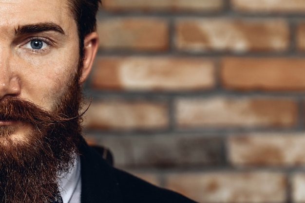 Foto ritratto del primo piano mezzo viso dell'uomo bello con i baffi e la barba che indossa la tuta. sullo sfondo di un muro di mattoni.