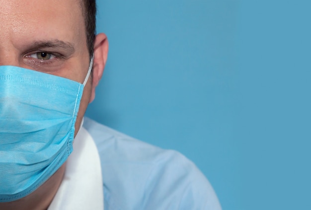 Half face detail of green eyes male nurse with disposable face mask and blue background